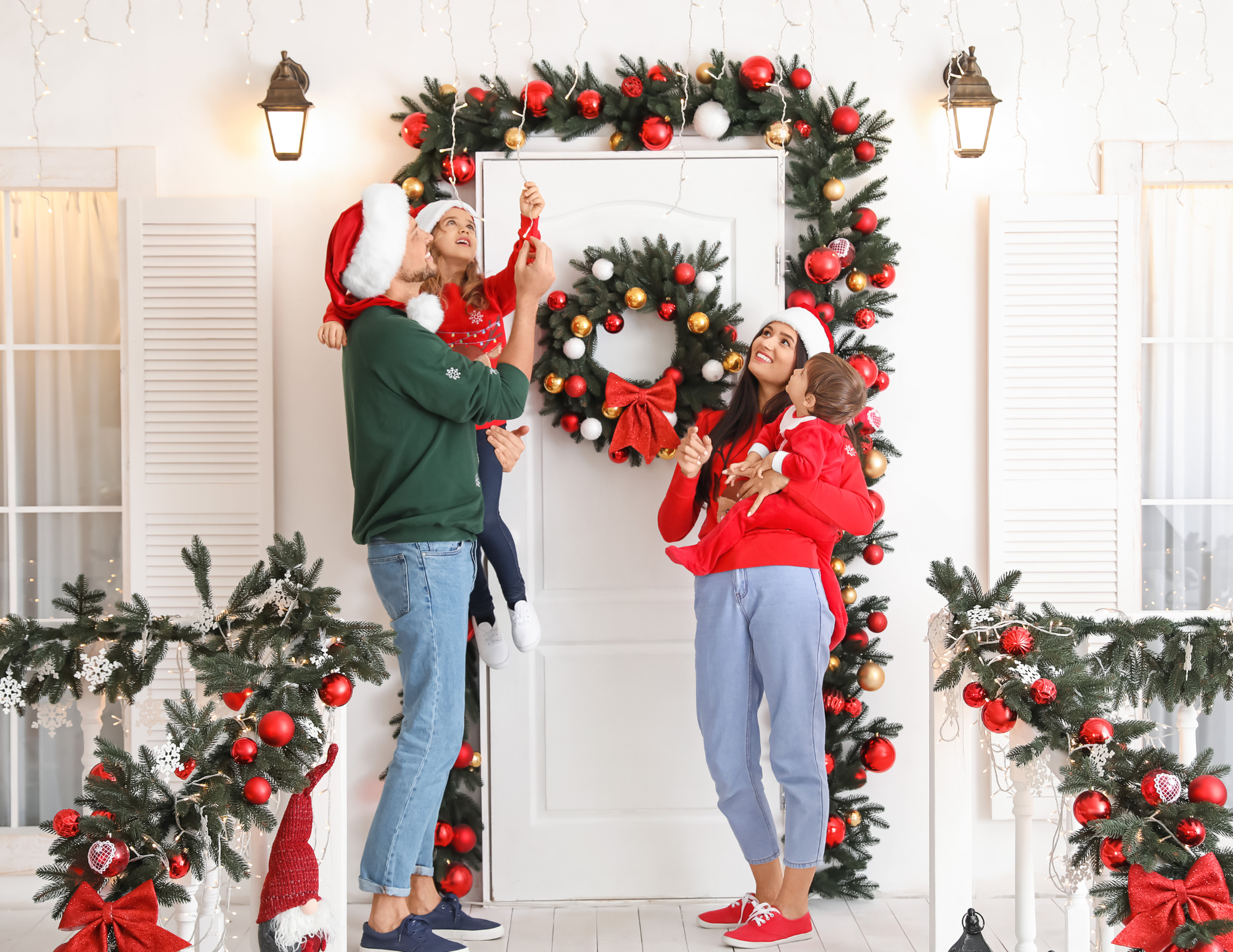 Family decorating their home's front porch with wreaths and holiday garlands.